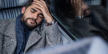 Man with headache or migraine holds head leaning against the vehicle window