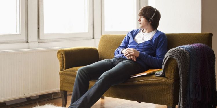 A teenage boy wearing headphones sitting on a couch